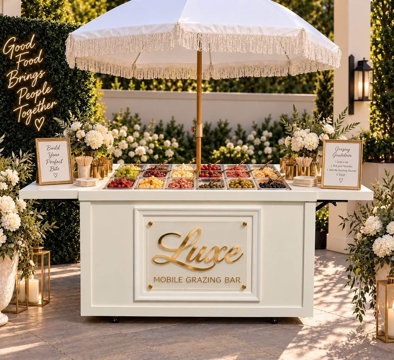 The Luxe mobile grazing bar cart styled outdoors with florals and a fringed umbrella
